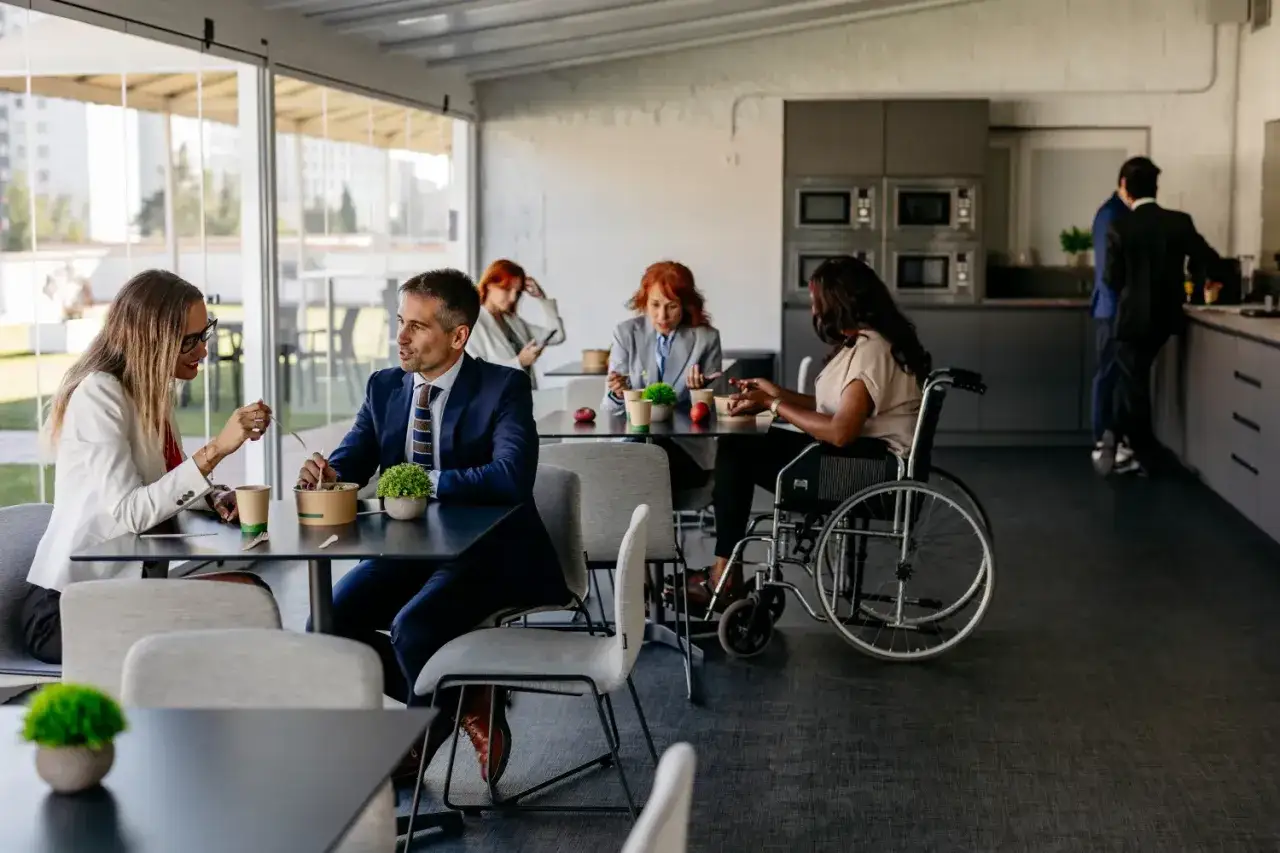 Des coll&egrave;gues profitent d'une pause repas, respectant le code du travail. Une femme en fauteuil roulant discute avec un homme, tandis que d'autres personnes mangent.