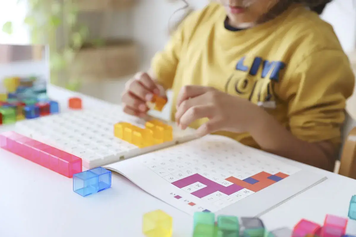 Ni&ntilde;a jugando con bloques de colores y un libro de **juegos de matem&aacute;ticas**.
