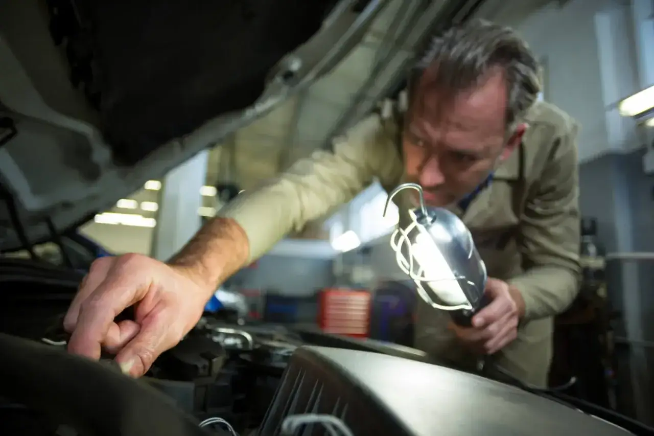 Mechanik z lampą inspekcyjną sprawdza, jak sprawdzić pompę sprzęgła w samochodzie.
