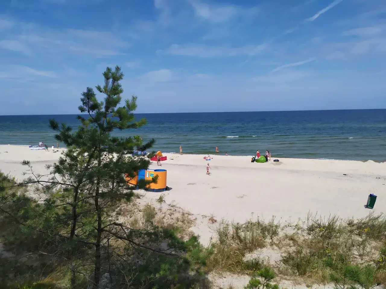 Słoneczna plaża między Grzybowem a Dźwirzynem. Widać ludzi, parawany i morze.