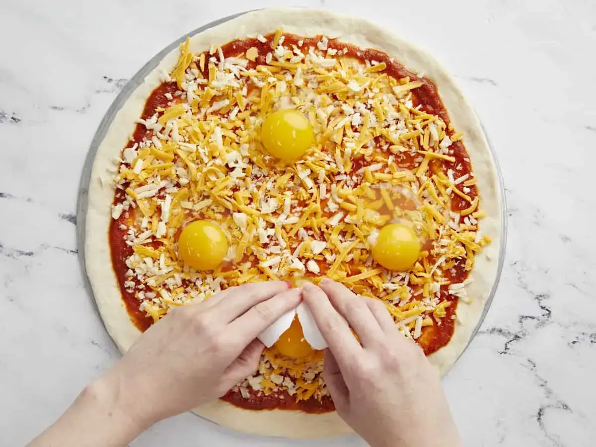 Ręce dodają jajko na pizzę z serem i sosem pomidorowym. To będzie pyszna pizza z jajkiem!