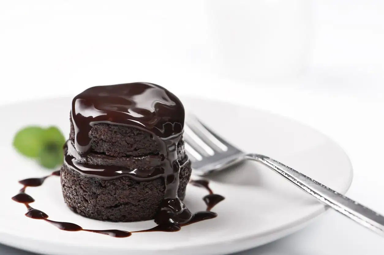 Pyszne muffinki brownie polane czekoladą, udekorowane listkiem mięty i polewą. Obok widelec.