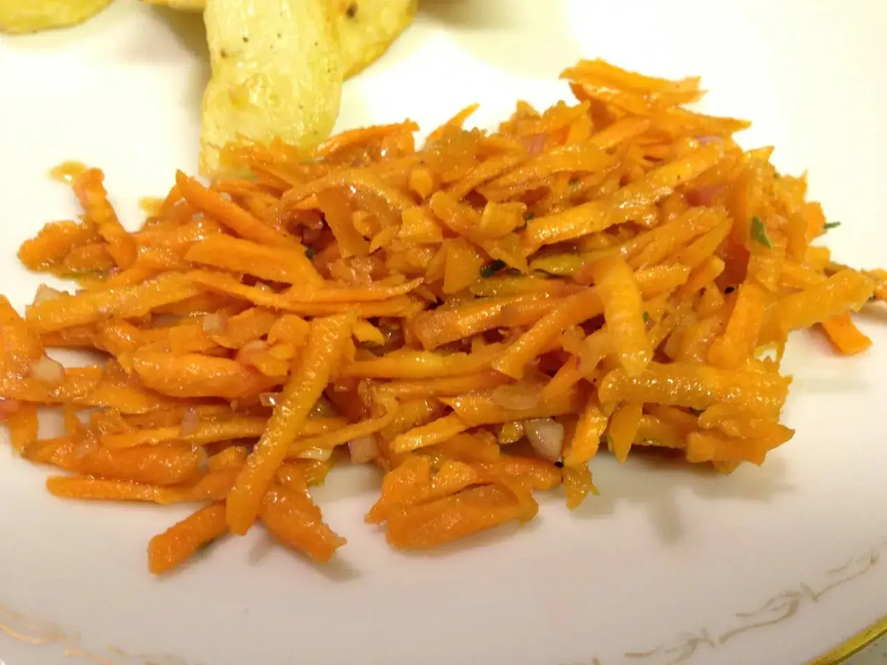 En fransk morotssallad med finstrimlad morot, lök och en lätt dressing. Serveras på en vit tallrik.