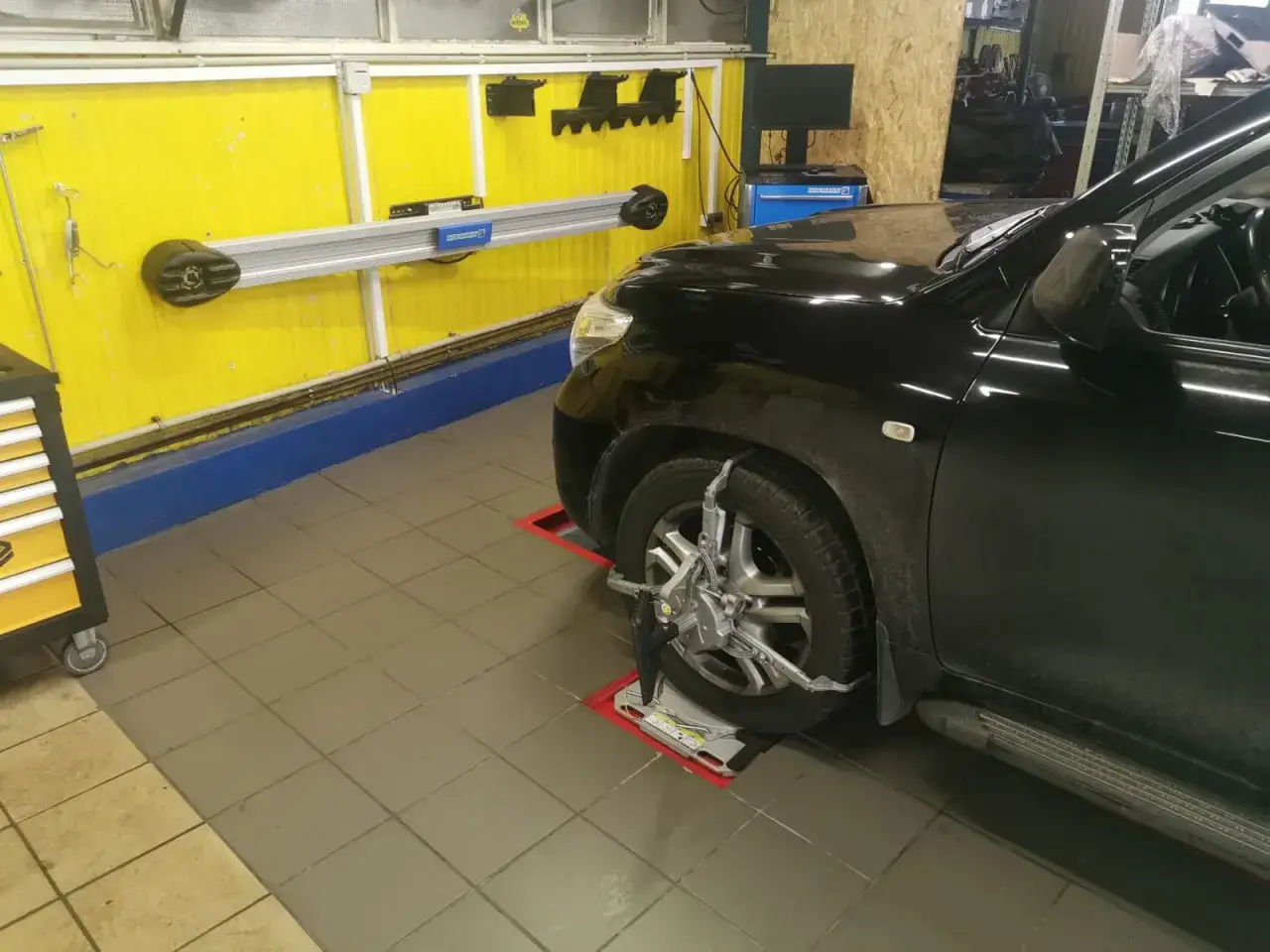 Czarny SUV na stanowisku do geometrii kół. Urządzenie do pomiaru zbieżności jest zamontowane na przednim kole. To pokazuje, ile trwa ustawienie zbieżności.