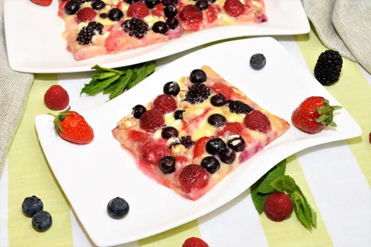 Eine süße Eiscreme Pizza mit frischen Beeren wie Himbeeren, Blaubeeren und Erdbeeren, garniert mit Minze.