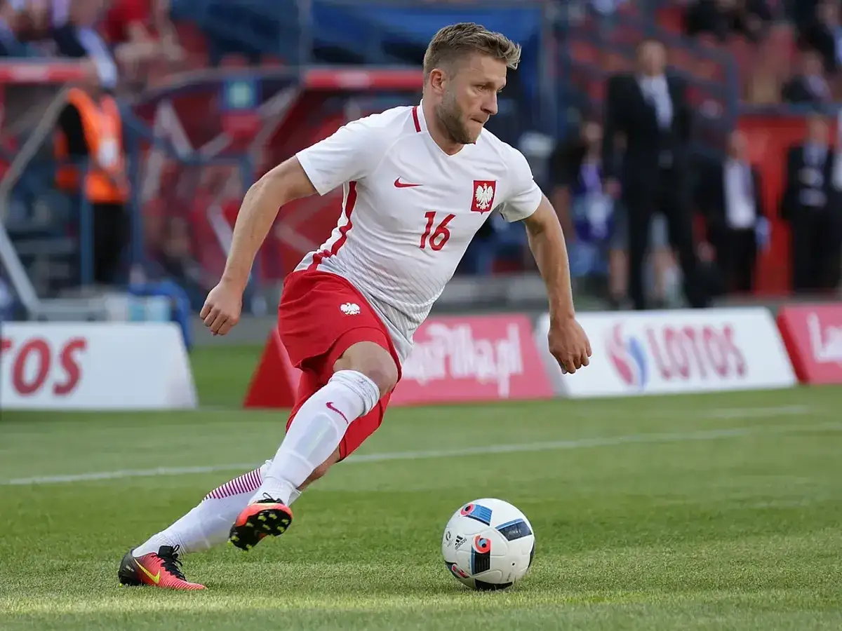 Piłkarz w białej koszulce z numerem 16, Jakub Błaszczykowski, z błyszczącym wzrostem formy, drybluje z piłką na boisku.