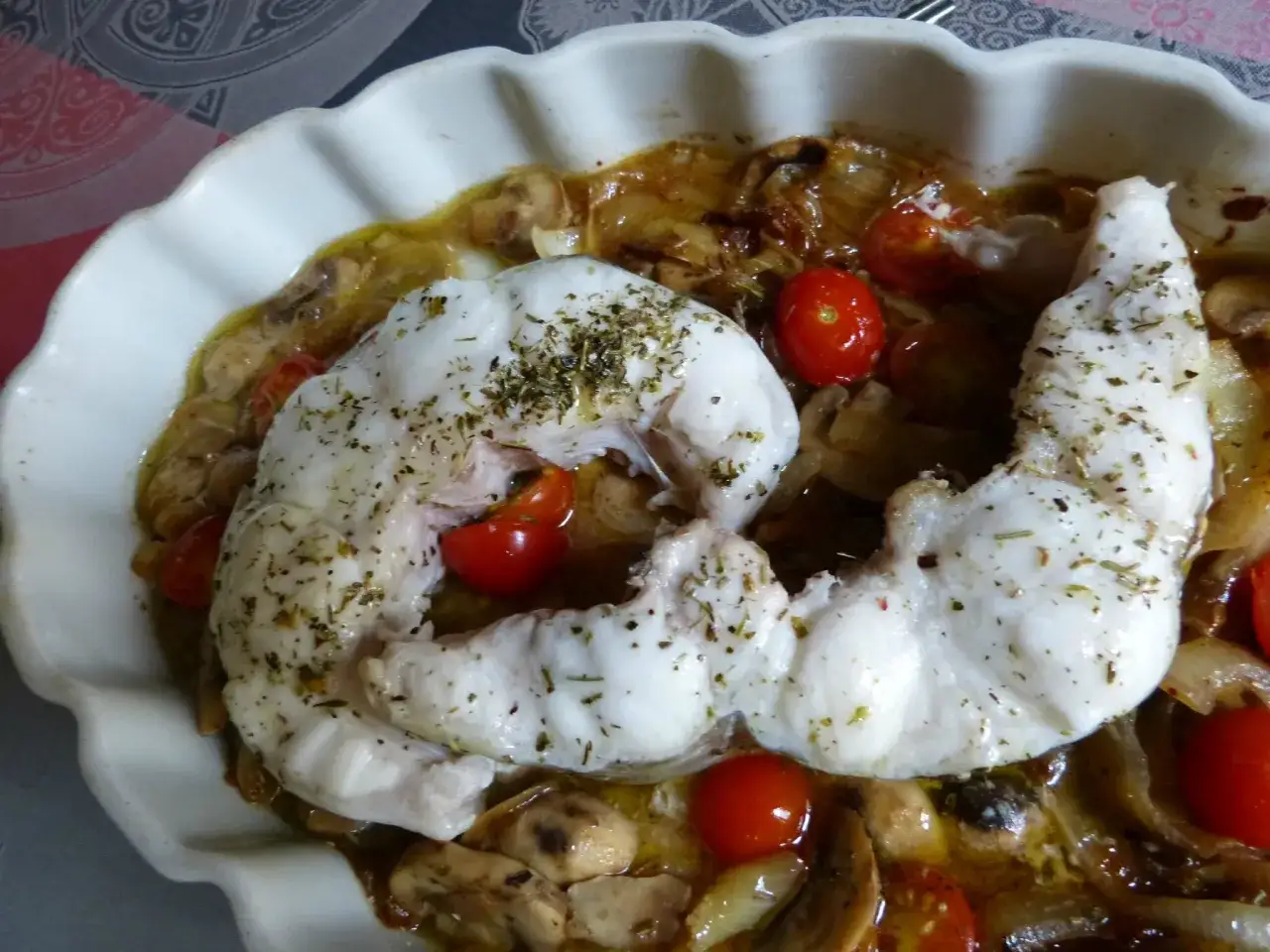 Un plat appétissant de filet de congre au four, garni de tomates cerises et de champignons, prêt à être dégusté.