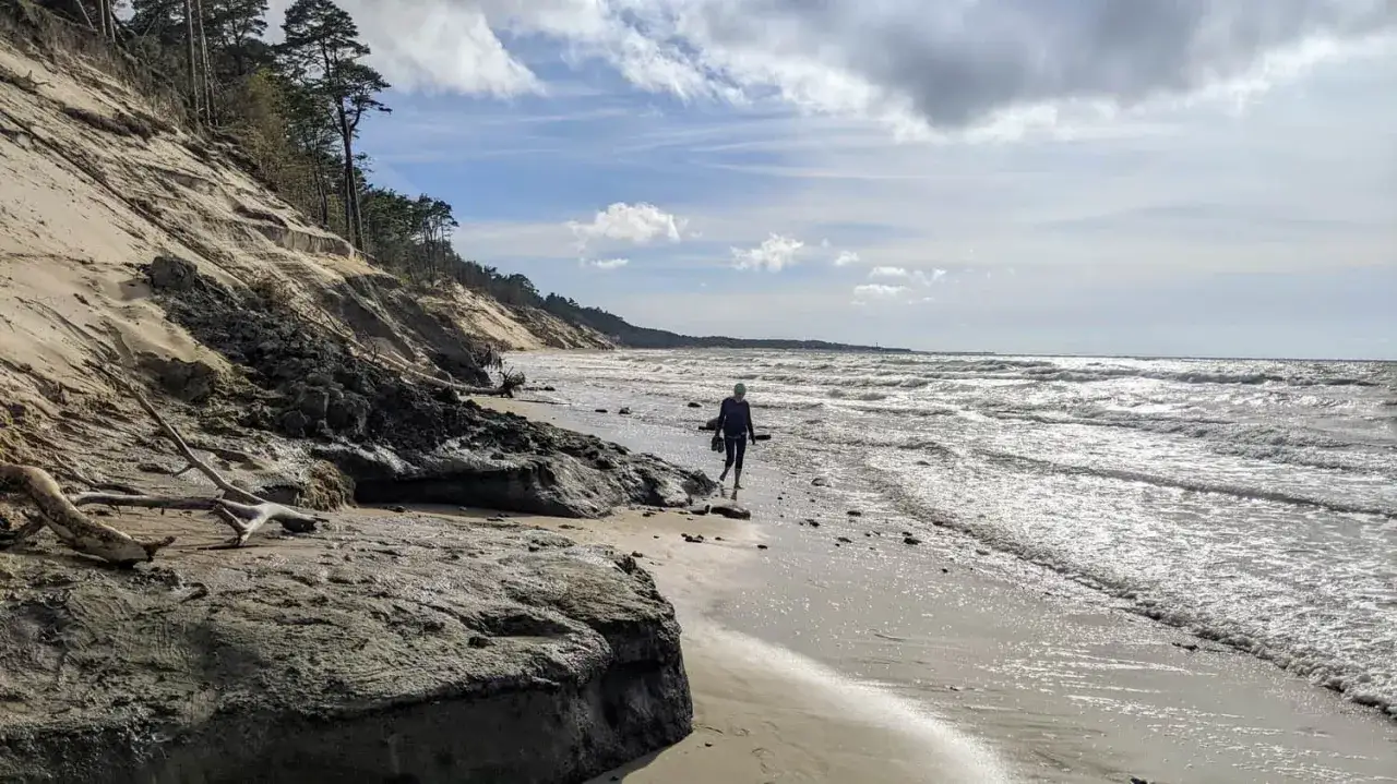 Spacerująca osoba na plaży w Ustce, w oddali widać klify. Odległość do morza jest niewielka, a plaża piaszczysta.