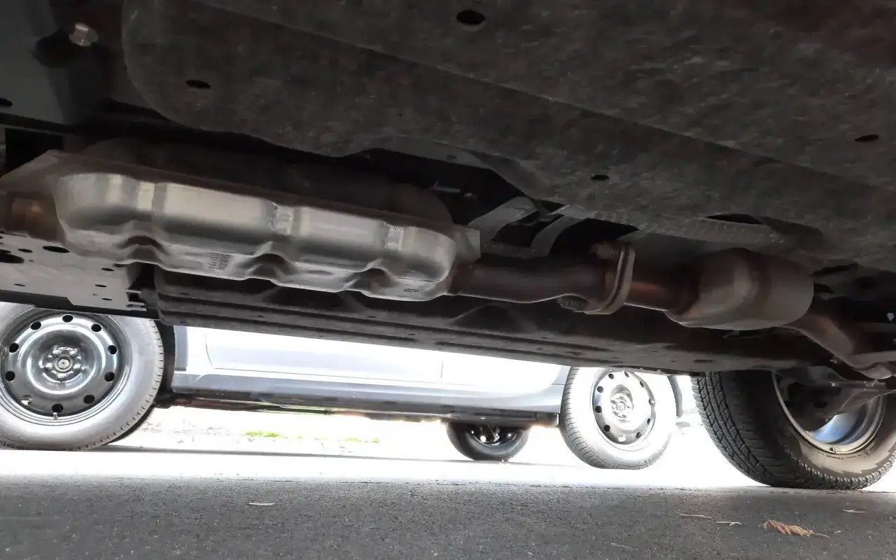 Vue sous une voiture montrant le syst&egrave;me d'&eacute;chappement, y compris le catalyseur. Un sympt&ocirc;me catalyseur HS essence peut causer des probl&egrave;mes de performance.