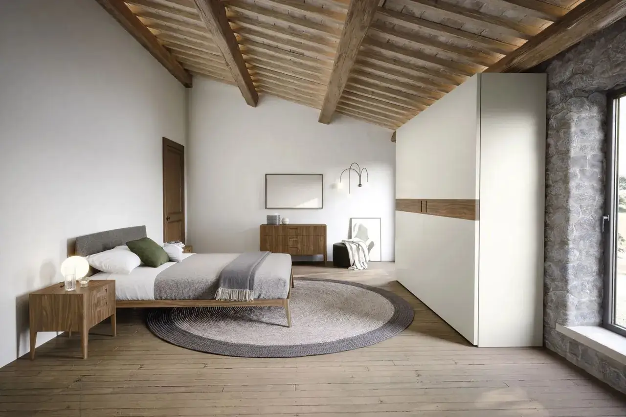 Habitaci&oacute;n r&uacute;stica con vigas de madera, cama acogedora, armario blanco y piedra natural. Un espacio que demuestra que las habitaciones peque&ntilde;as pueden ser muy acogedoras.