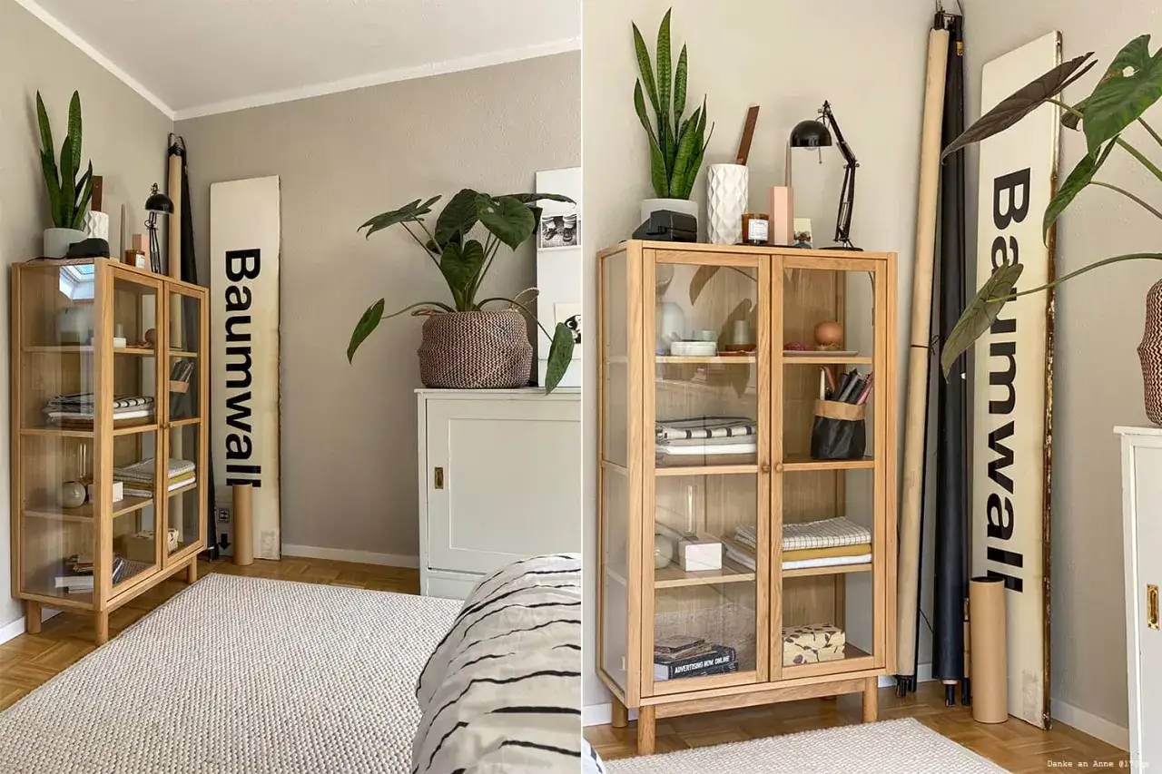 Beige Wände und ein heller Teppich schaffen eine warme Atmosphäre. Ein Holzschrank mit Glasfronten und Pflanzen runden das Bild ab.