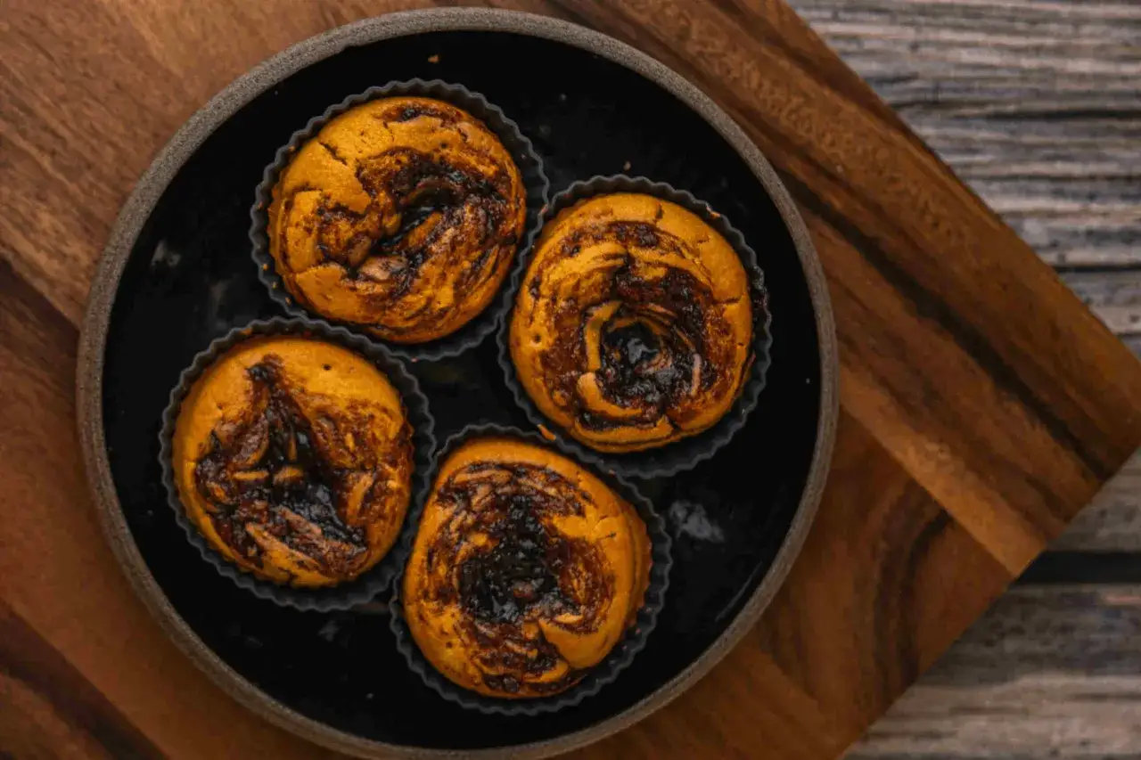Cztery muffiny z powidłami śliwkowymi, pieczone w ciemnych foremkach, ułożone na czarnym talerzu.