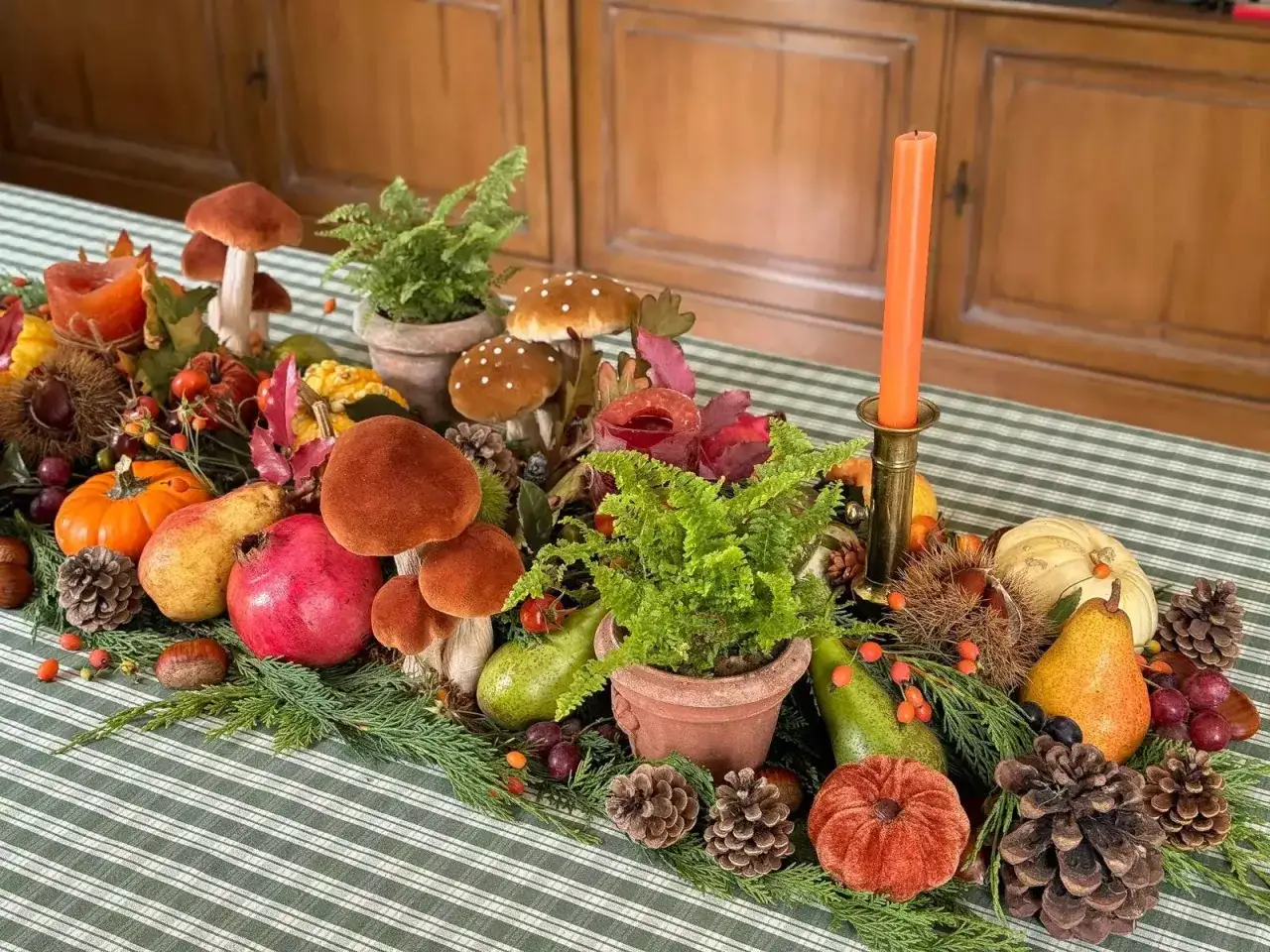 D&eacute;coration automnale sur une nappe &agrave; rayures vertes et blanches, avec des champignons, des citrouilles, des poires, des grenades et des foug&egrave;res, &eacute;voquant de belles couleurs automnales.