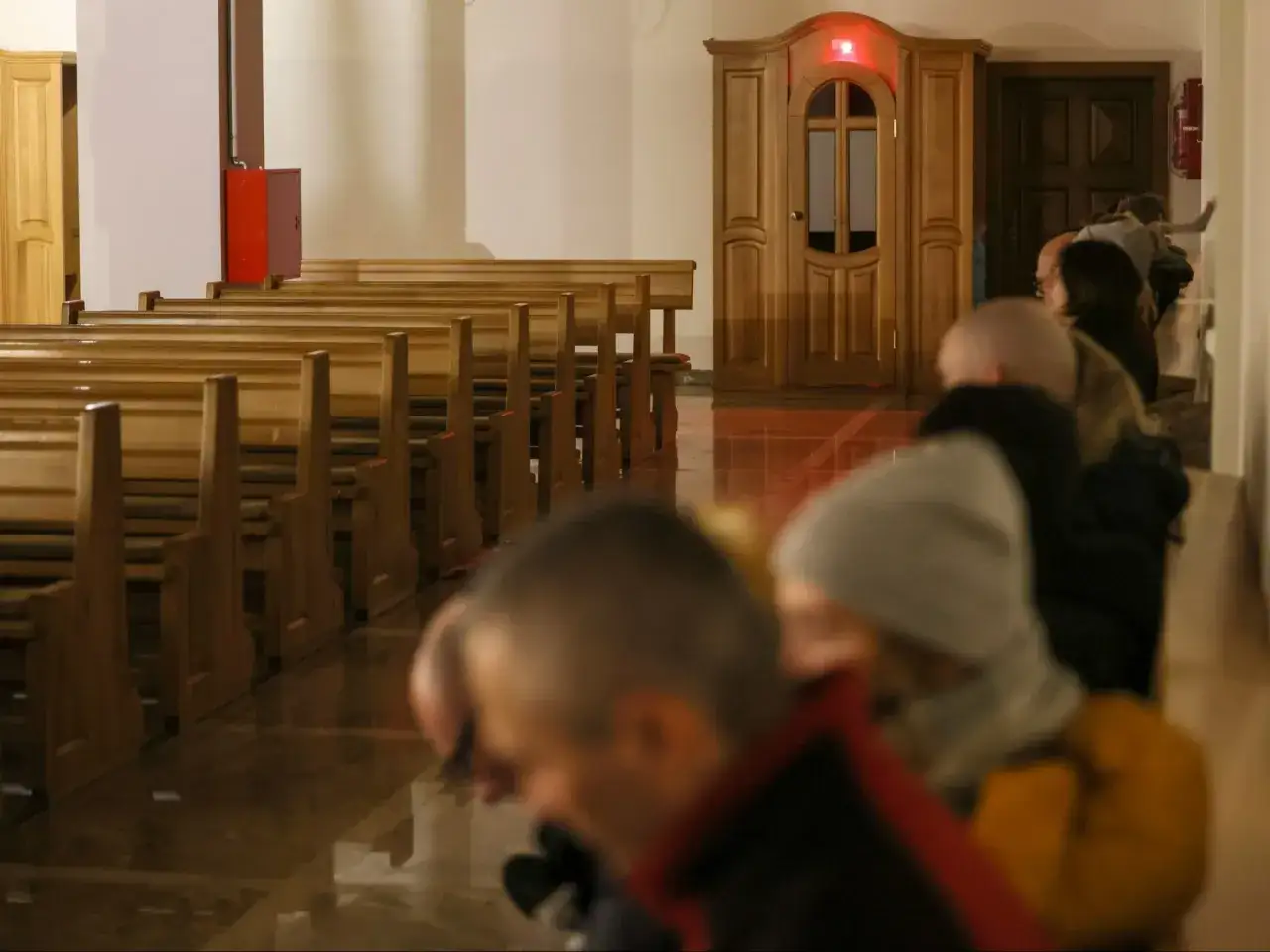 Ludzie w kościele czekają na spowiedź, szukając odpuszczenia grzechów. W tle widać konfesjonał.