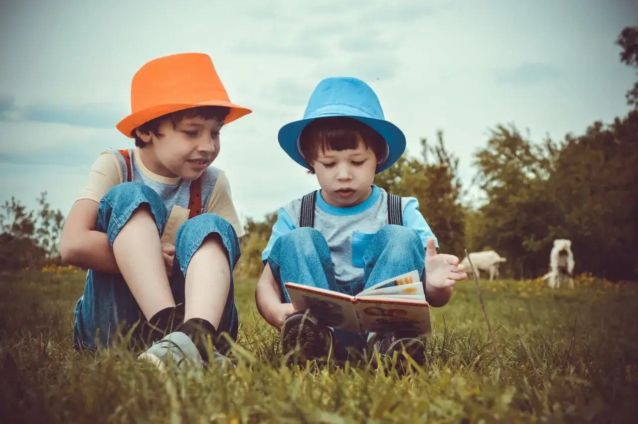 Dos ni&ntilde;os con sombreros de colores leen un libro de poemas para ni&ntilde;os de 7 a 8 a&ntilde;os sentados en la hierba.