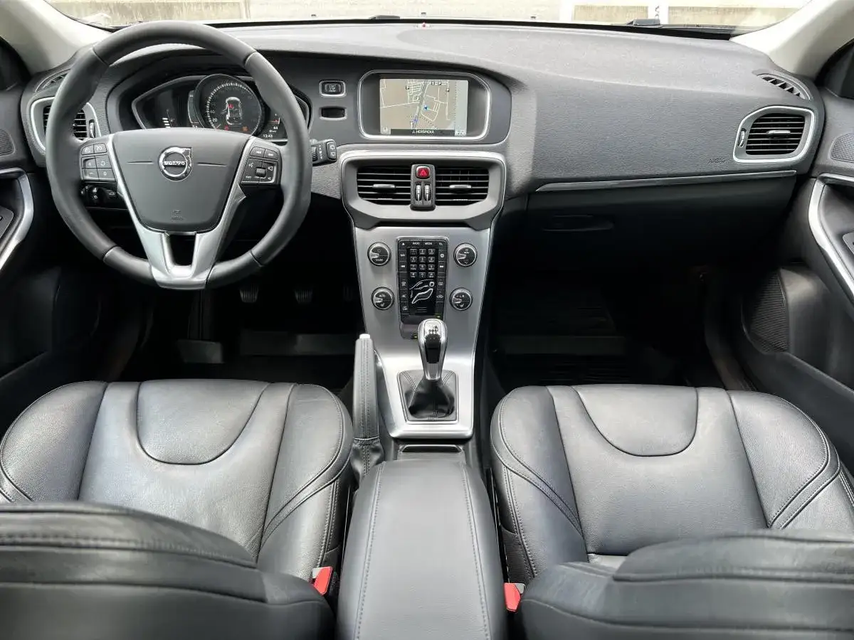 Wnętrze Volvo V40 D2: czarna skórzana tapicerka, kierownica, deska rozdzielcza z nawigacją i dźwignia zmiany biegów.