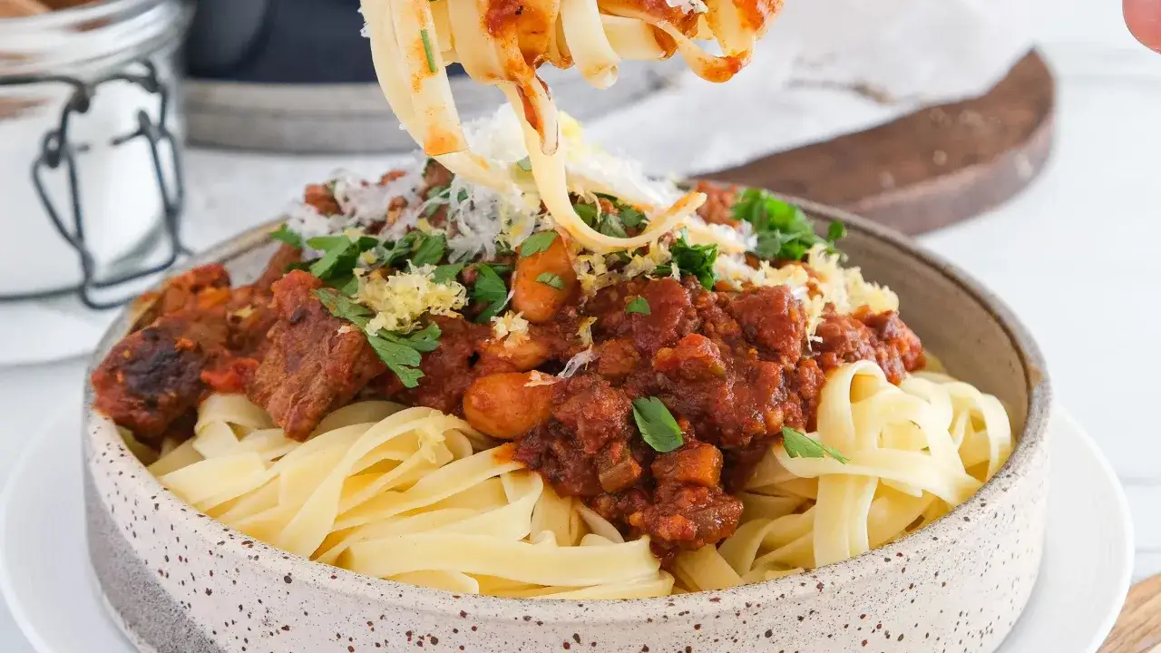 Ein Teller mit Tagliatelle, bedeckt mit einer reichhaltigen, traditionellen Bolognese-Sauce, garniert mit Parmesan und Petersilie.