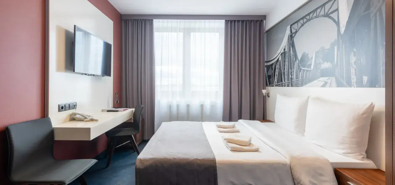 Pokój hotelowy z łóżkiem, biurkiem i TV. 