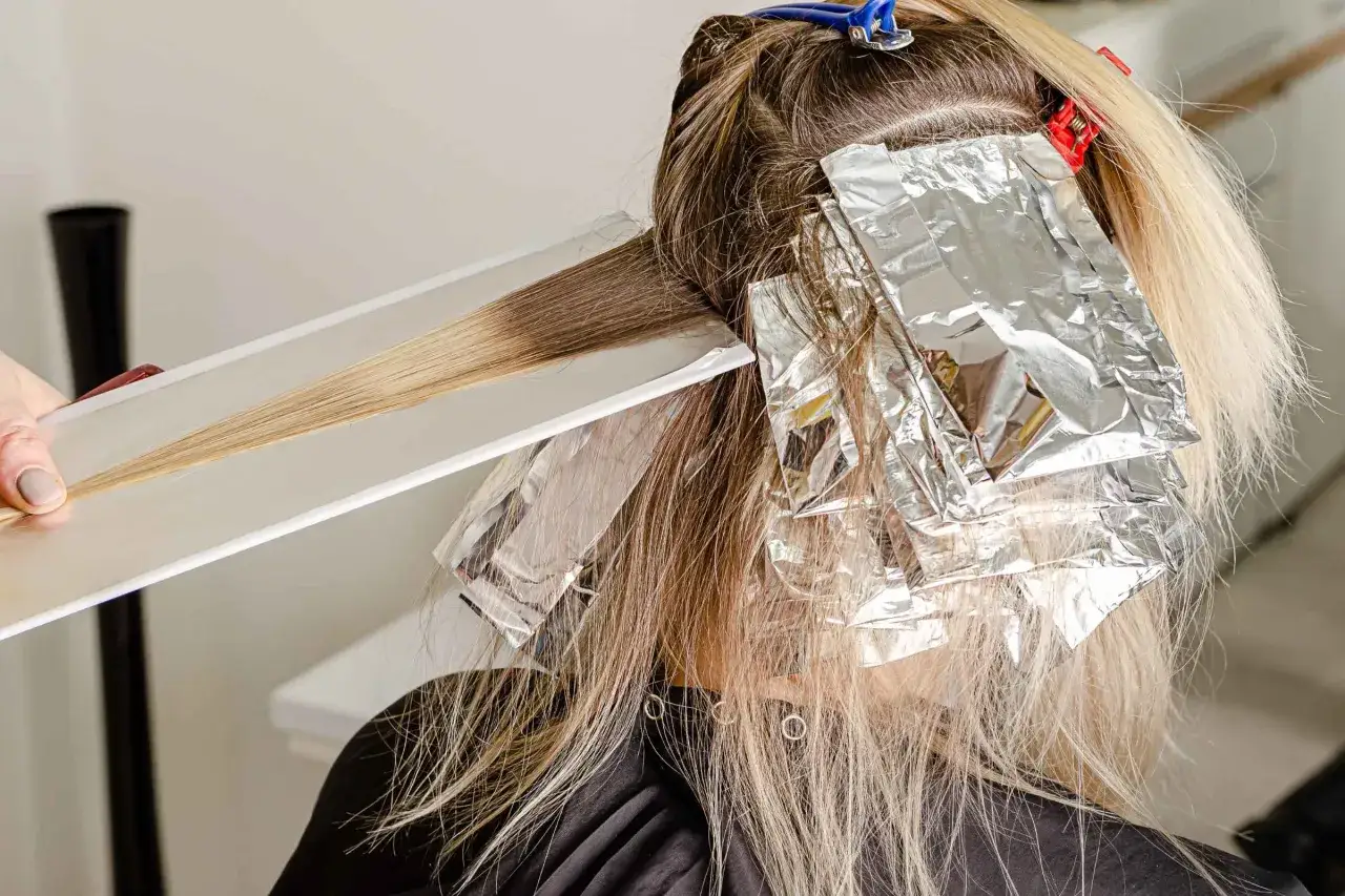 Capelli decolorati con tecnica a balayage, ciocche avvolte in stagnola per un effetto biondo luminoso.