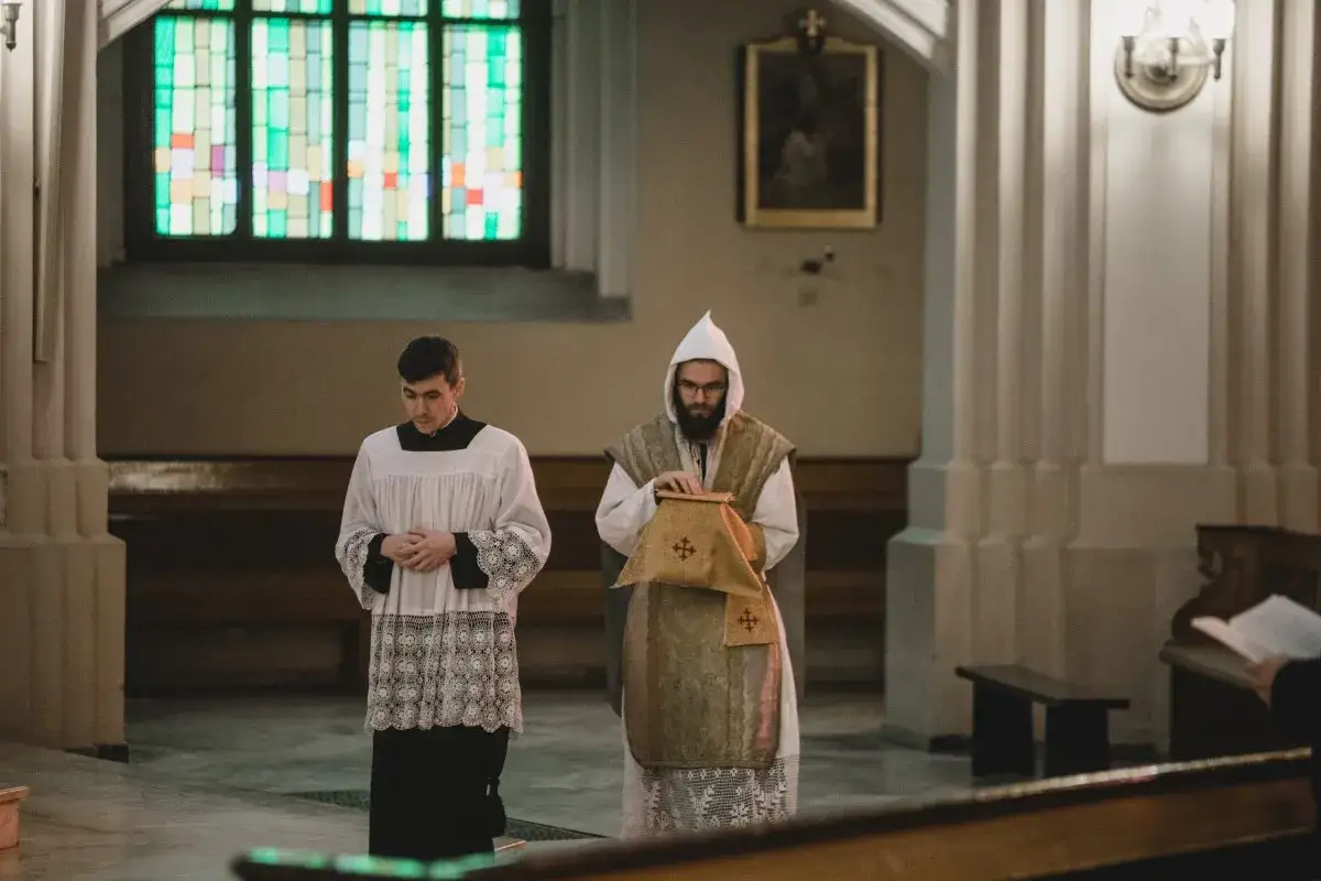 Dwóch mężczyzn w szatach liturgicznych. Jeden w albie i czarnej sutannie, drugi w białej komży i ozdobnej kapie. Przygotowania do mszy trydenckiej jak się ubrać.