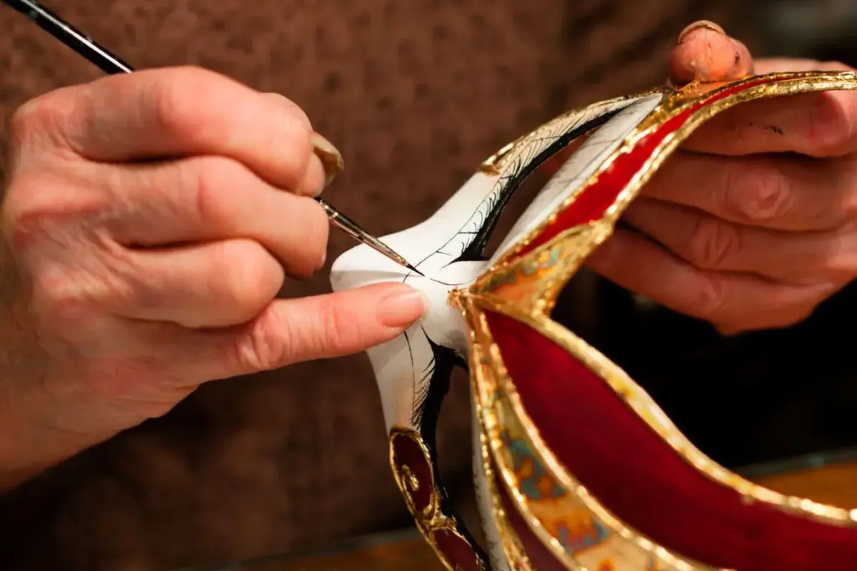 Mani esperte dipingono dettagli su una maschera, un esempio di artigianato locale che prende vita con cura e passione.