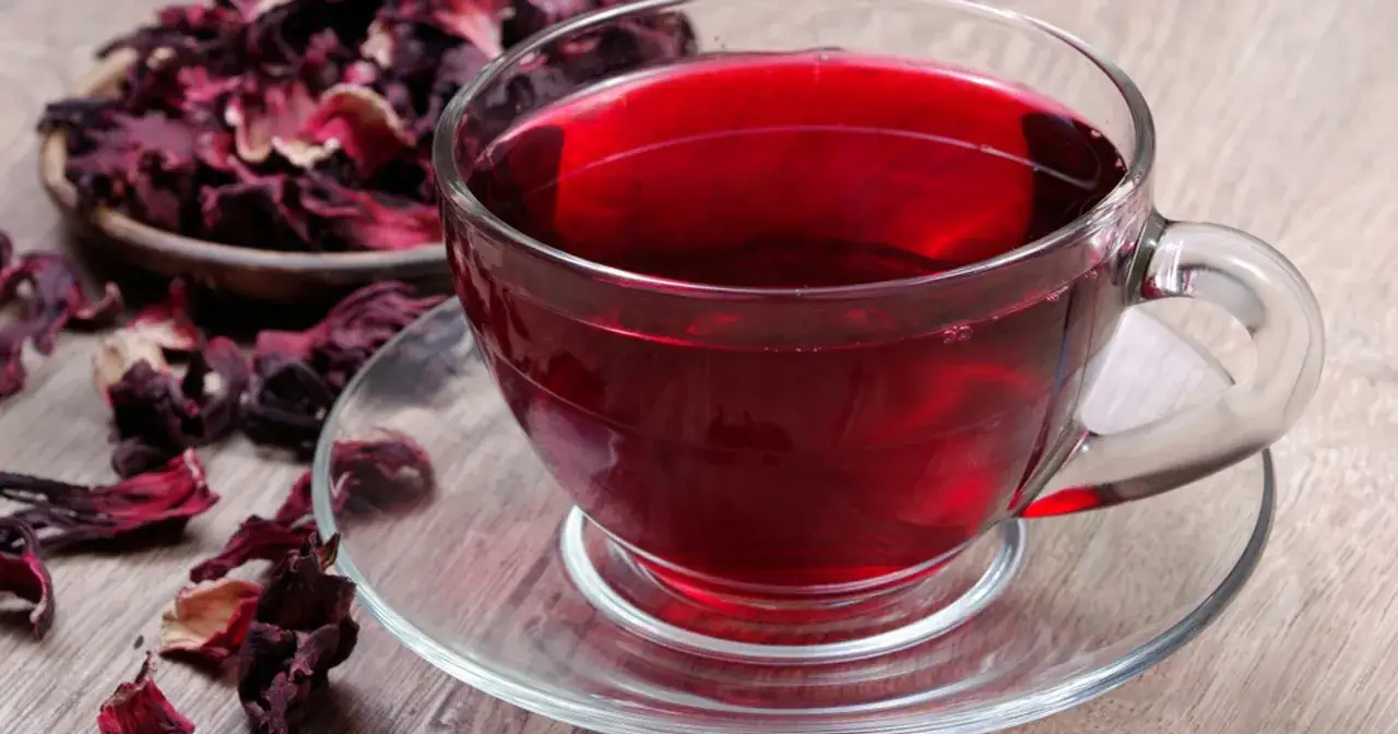 Aromatyczna herbatka z hibiskusa w szklanej filiżance, obok miseczki z suszonymi kwiatami.
