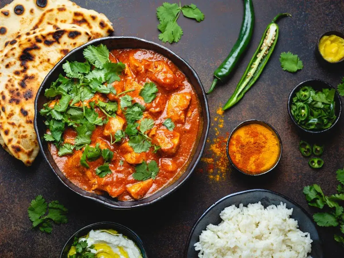 Aksamitne curry z kurczaka, podane z ryżem, plackami naan i świeżą kolendrą. Obok zielone papryczki chili i przyprawy.