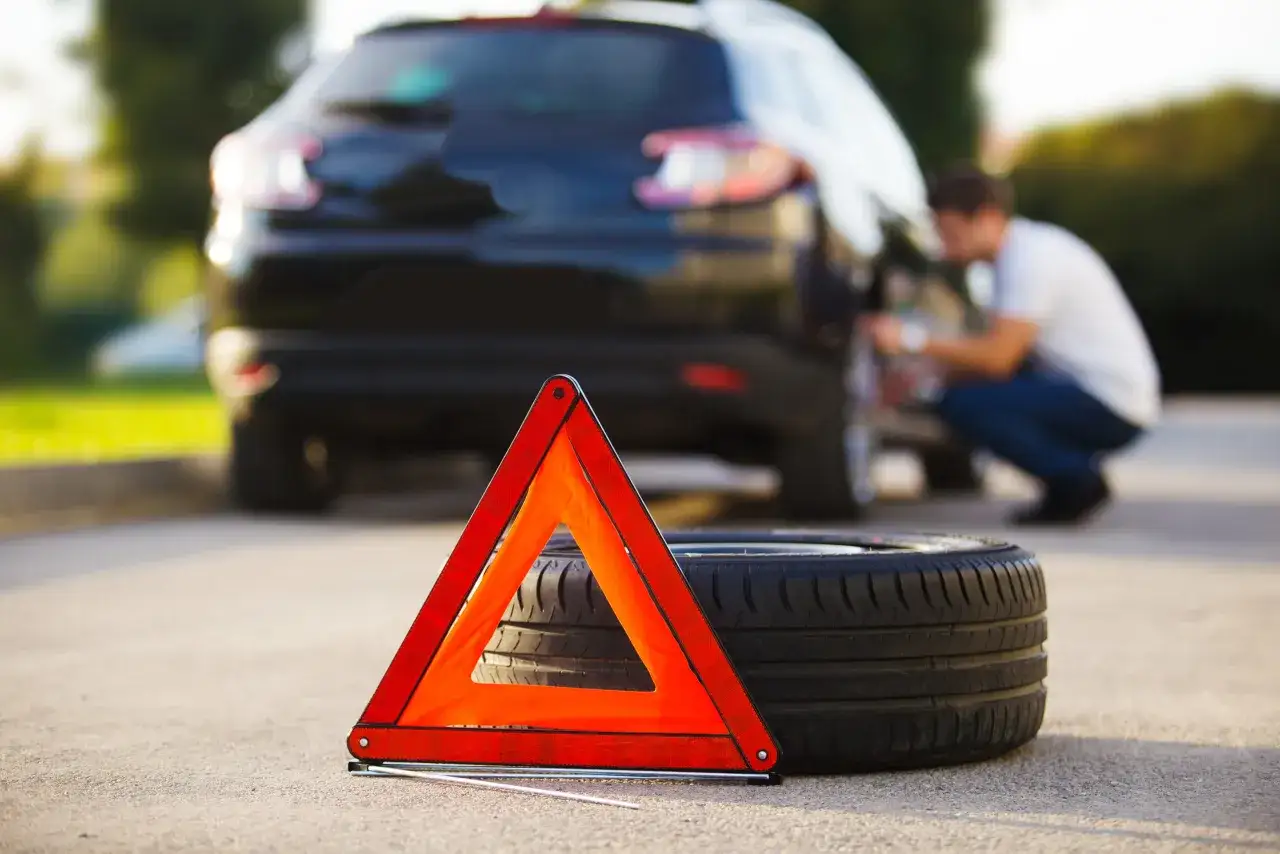 Triangolo di emergenza e ruota a terra accanto a un'auto. La domanda &egrave;: in quanto tempo si sgonfia una gomma bucata?