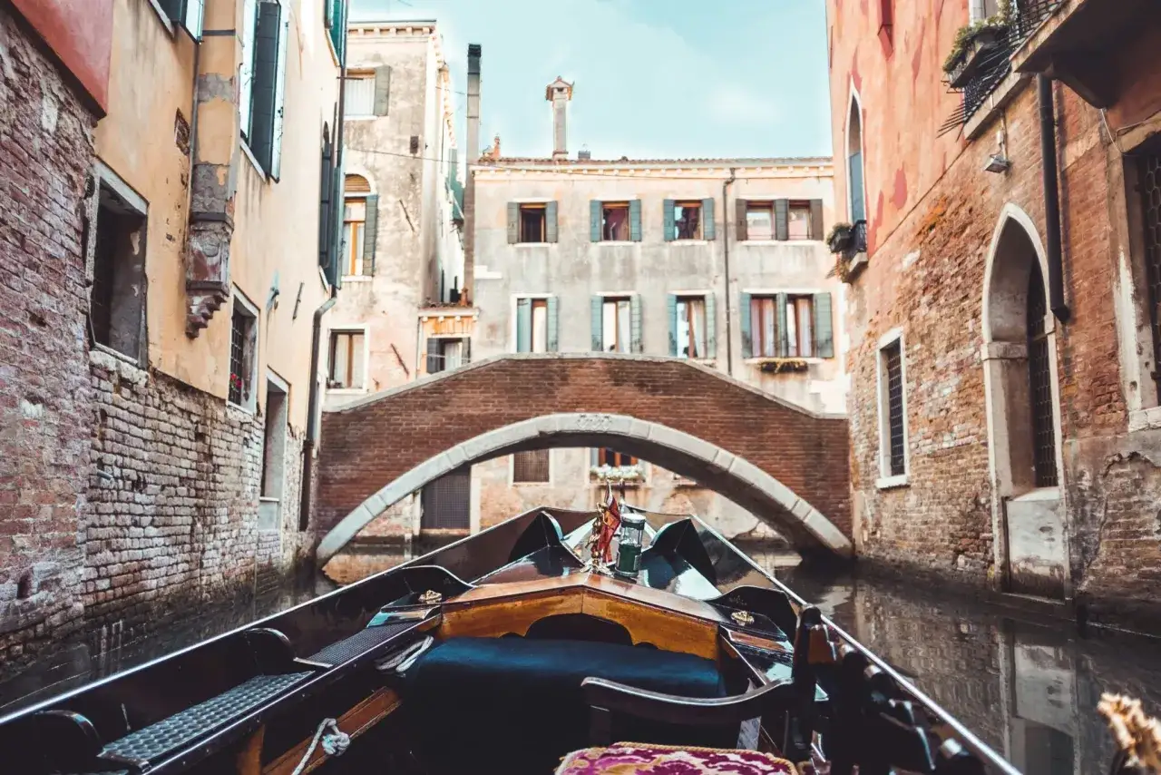 Gondola in un canale di Venezia, la Serenissima, con un ponte in mattoni sullo sfondo.