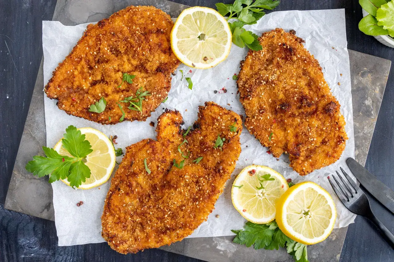 Drei goldbraune Schnitzel im Backofen, garniert mit Zitronenspalten und Petersilie.