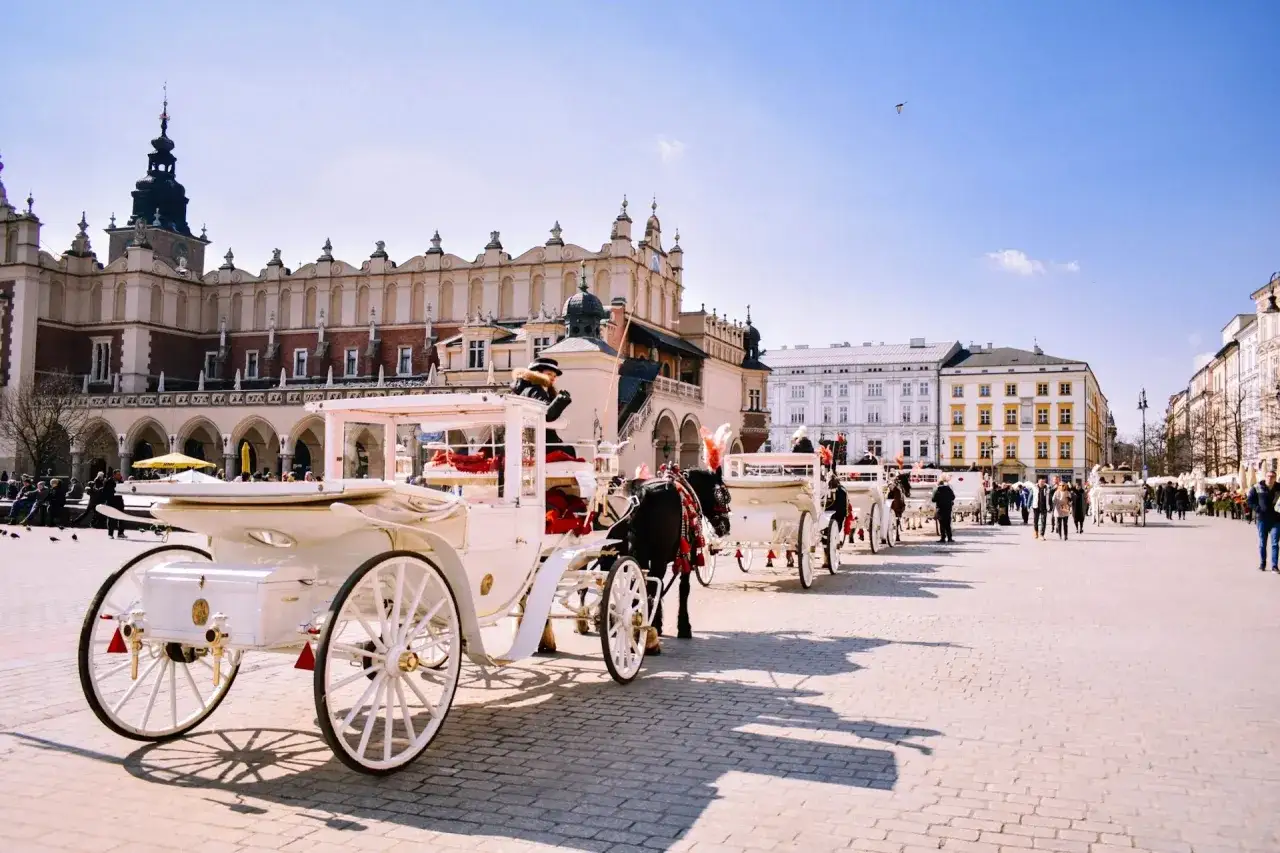 Krak&oacute;w Rynek atrakcje: białe dorożki czekają na turyst&oacute;w na brukowanym placu przed Sukiennicami.