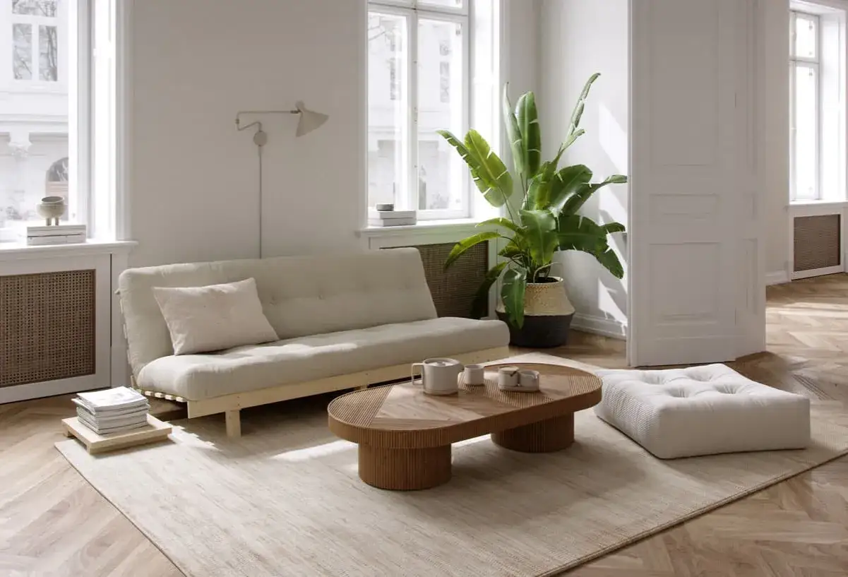Un **salon Japandi** lumineux avec un canap&eacute; beige, une table basse en bois organique, une plante verte luxuriante et un pouf moelleux sur un tapis textur&eacute;.