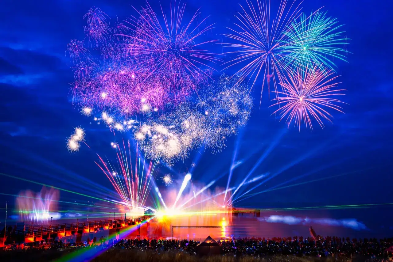 Spektakuläres Feuerwerk über dem Meer, Menschen feiern Silvester am Meer mit bunten Lichtern und Explosionen am Himmel.