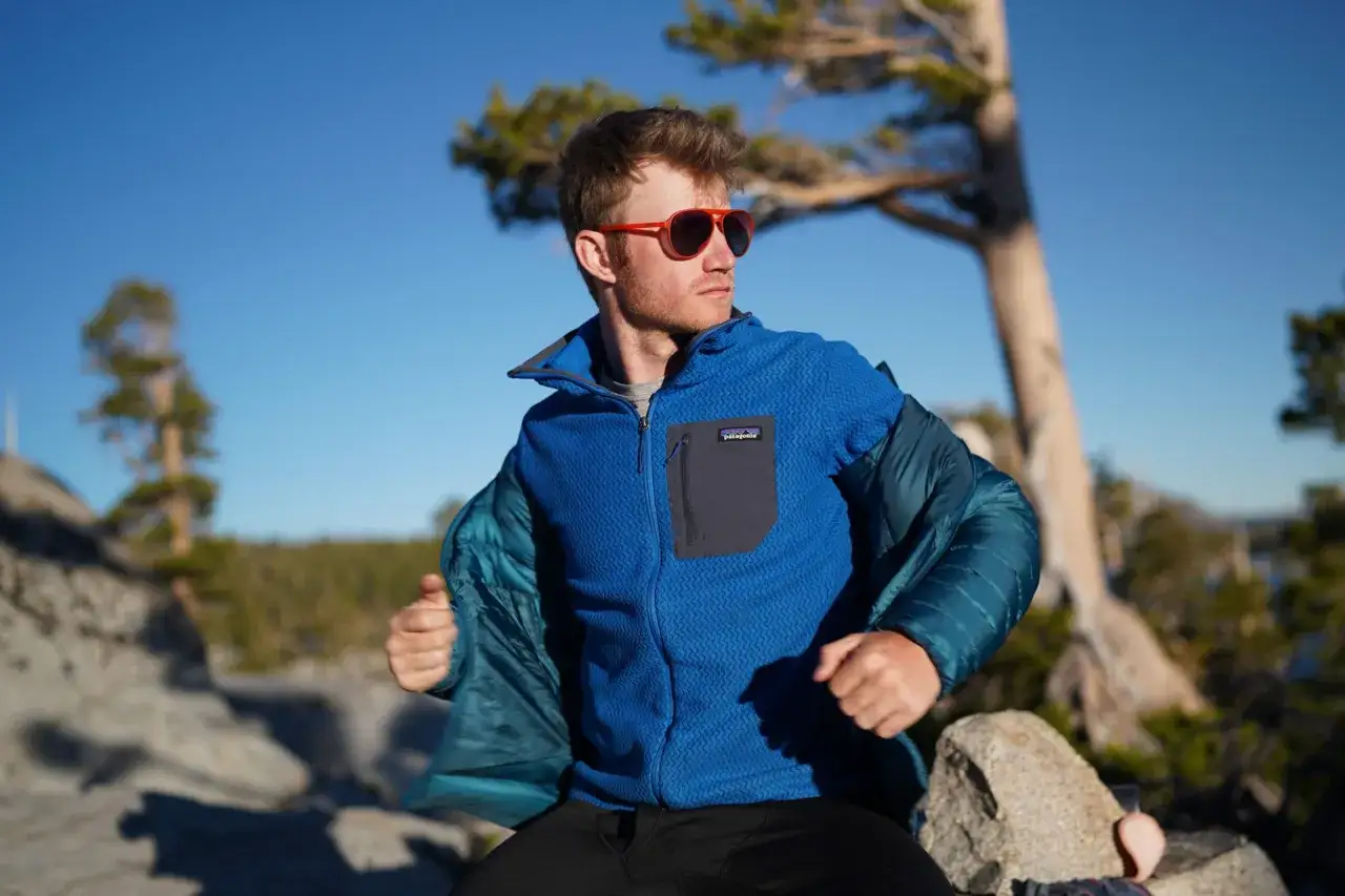 Ein Mann mit roten Sonnenbrillen zieht seine blaue Fleecejacke an. Sie ist warm und perfekt f&uuml;r Outdoor-Abenteuer.