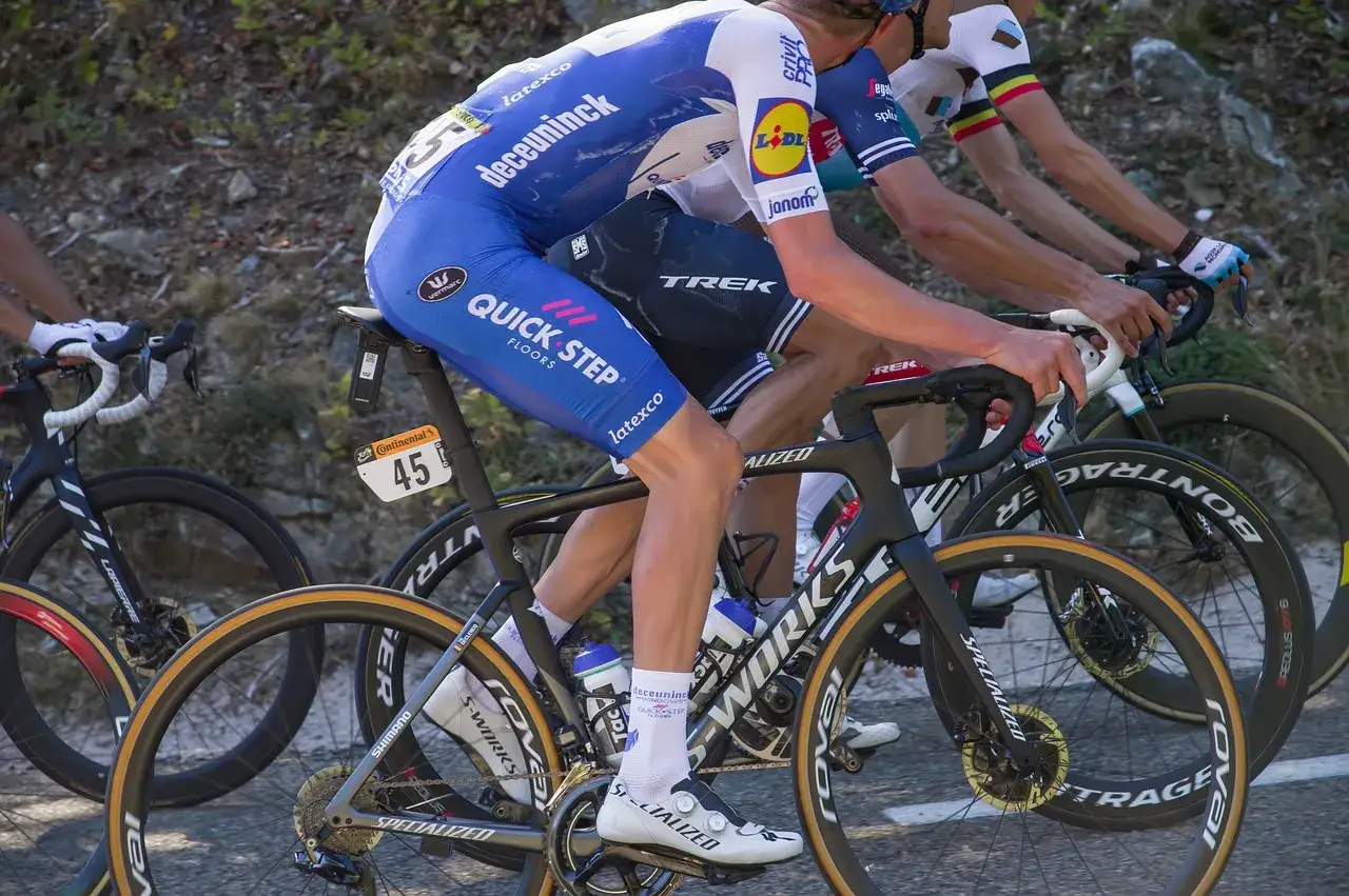Cyclists in blue and white jerseys on specialized tour de france training bikes, racing uphill.