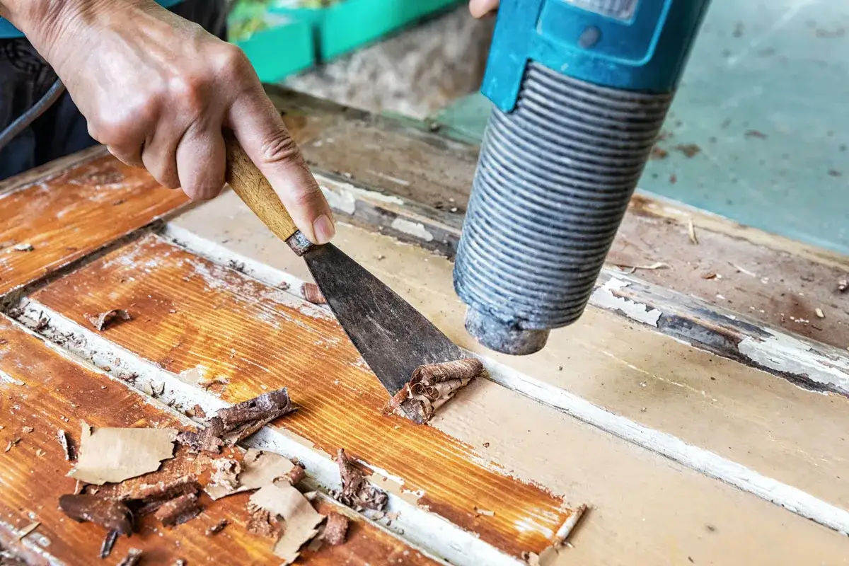 Alte Farbe wird mit einem Hei&szlig;luftgebl&auml;se und Spachtel von Holz entfernt.