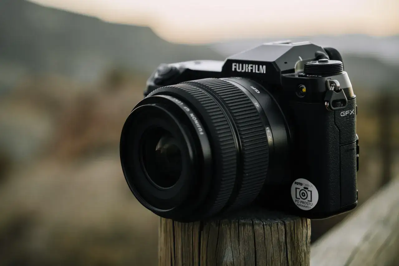Aparat Fujifilm GFX 50s II z obiektywem na drewnianym słupku.