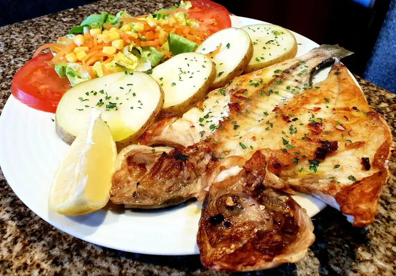 Un delicioso plato de pescado a la plancha con patatas, ensalada y limón. Una experiencia culinaria perfecta para comer en Muxía.