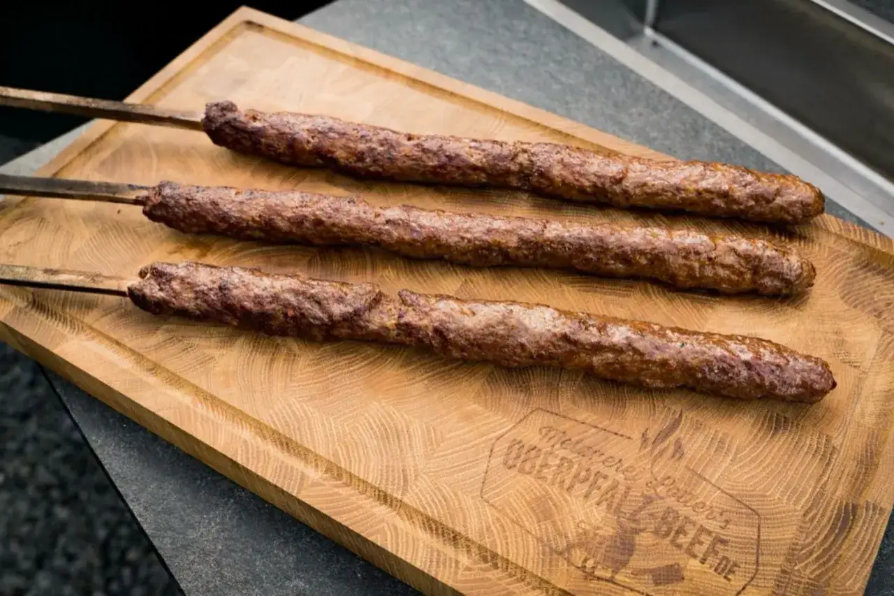 Drei saftige Adana Kebabs auf einem Holzbrett, bereit f&uuml;r ein k&ouml;stliches Adana Kebap Rezept.