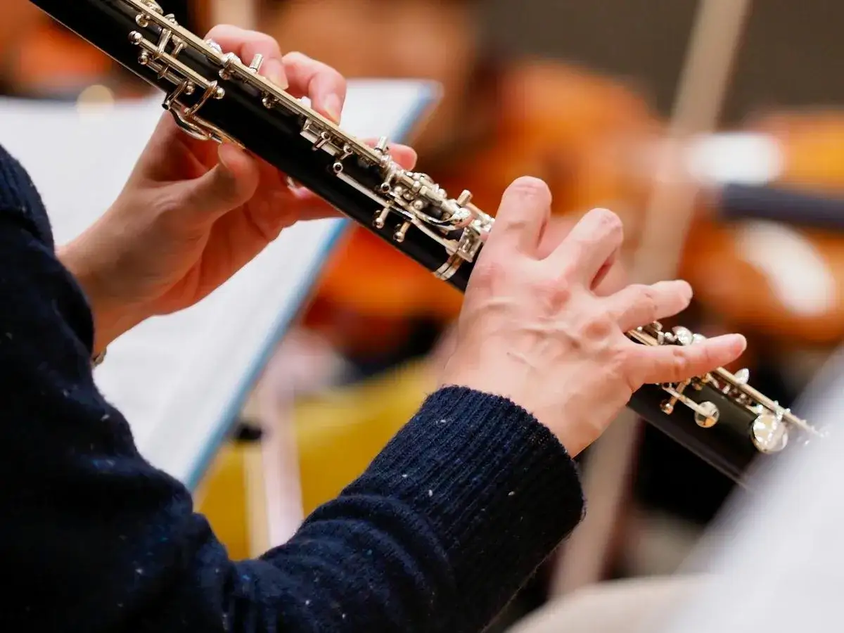 Mains délicates jouant d'un instrument à vent, un hautbois, dans un orchestre. Les clés argentées brillent sous la lumière.