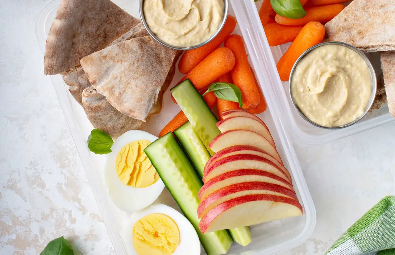 Pyszne i zdrowe przekąski: jajka na twardo, pokrojone jabłko, marchewki, ogórek, pita i hummus. Idealne na lunchbox!