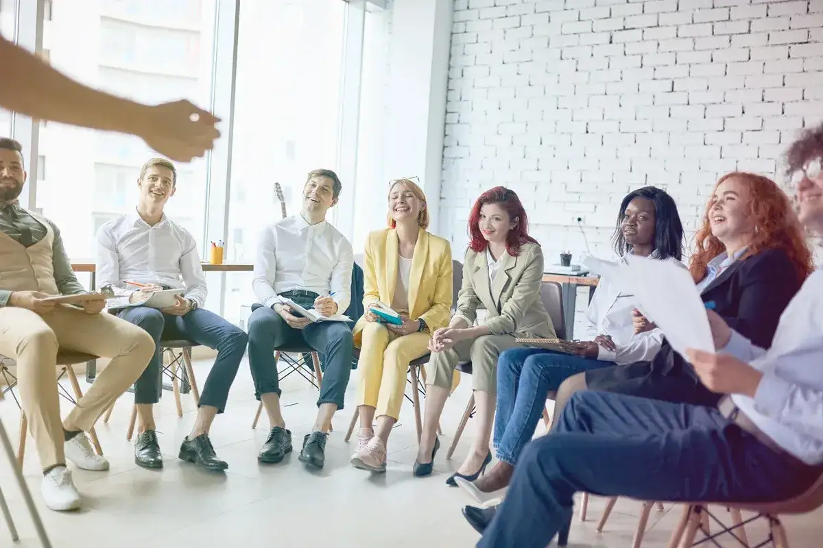 Diverse group engaged in lively group coaching session, smiling and interacting in a bright, modern room.