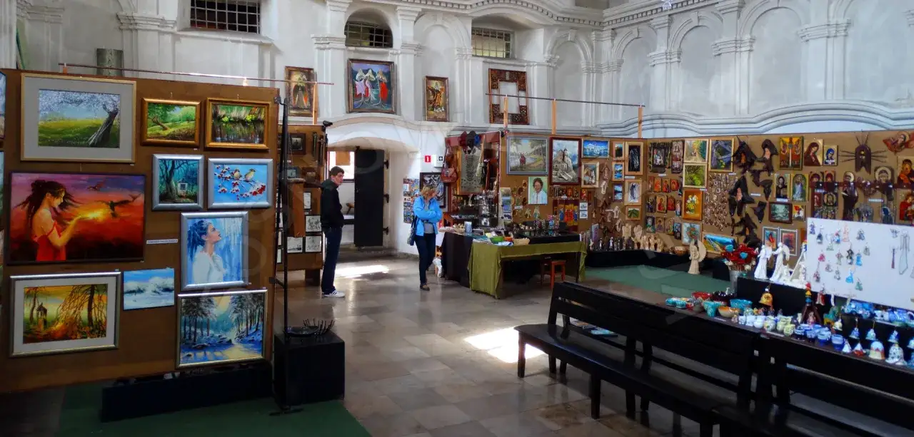 Wnętrze synagogi zamienione na galerię sztuki. Wystawa obrazów i rękodzieła, z ludźmi oglądającymi dzieła.