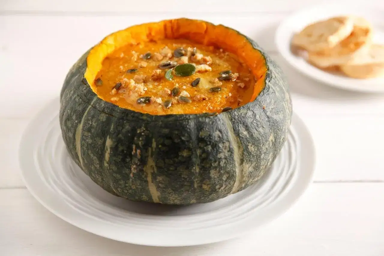 Vellutata di zucca servita in una zucca intagliata, guarnita con semi e crostini.