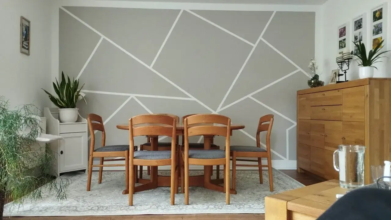 Esszimmer mit Holztisch und St&uuml;hlen vor einer Wand mit modernem, geometrischem Wandfarbe Muster in Grau und Wei&szlig;.