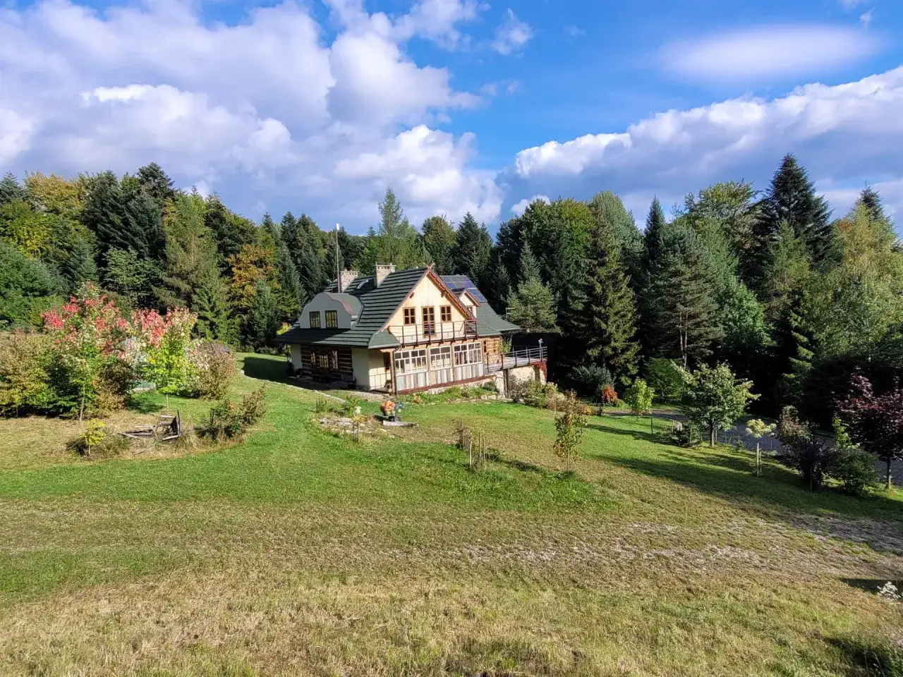 Drewniany dom w otoczeniu lasu, typowy dla beskidzkich miejscowości. Jesienne barwy drzew dodają uroku krajobrazowi.
