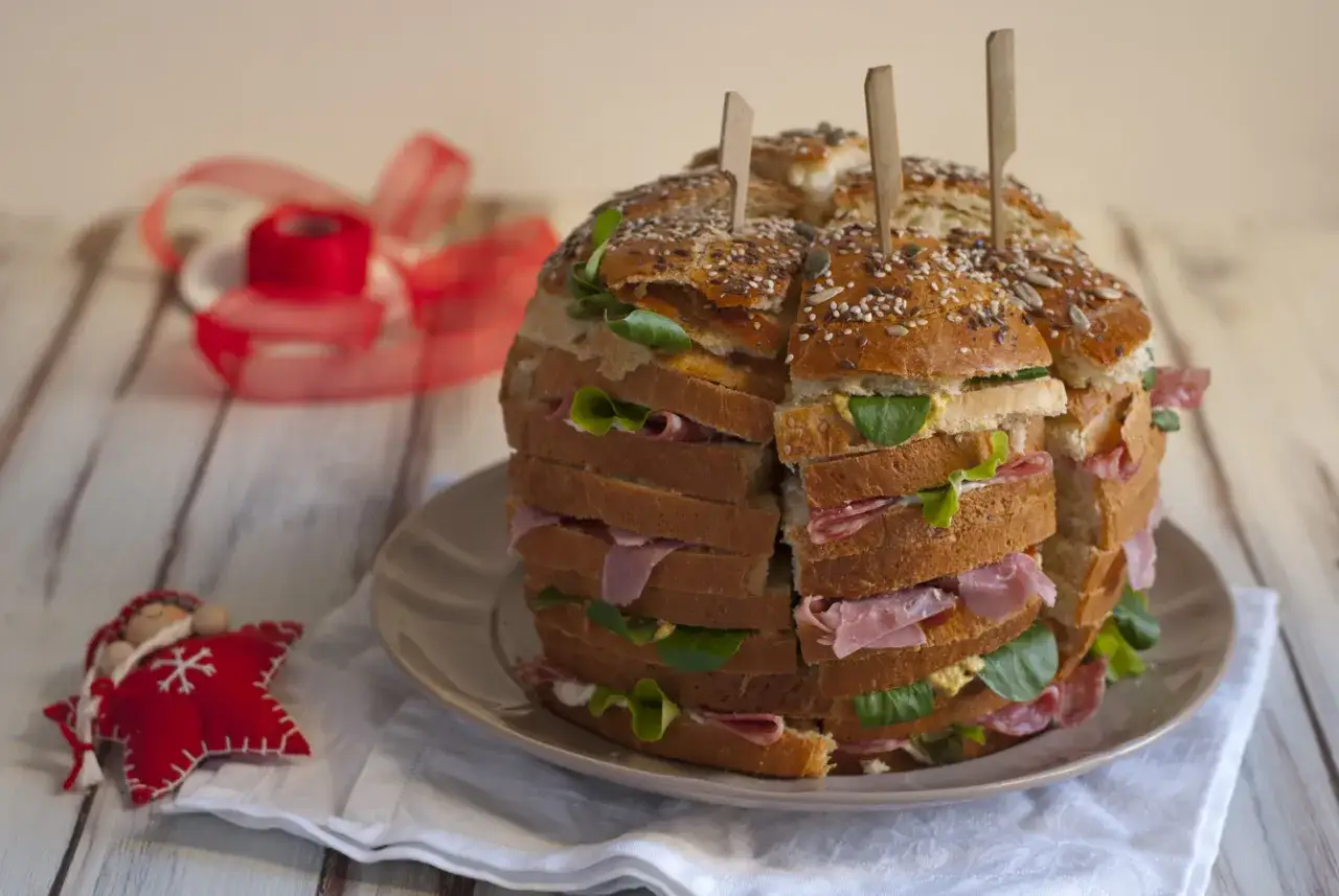 Un maestoso pane gastronomico a più strati, farcito con salumi e insalata, pronto per una festa.