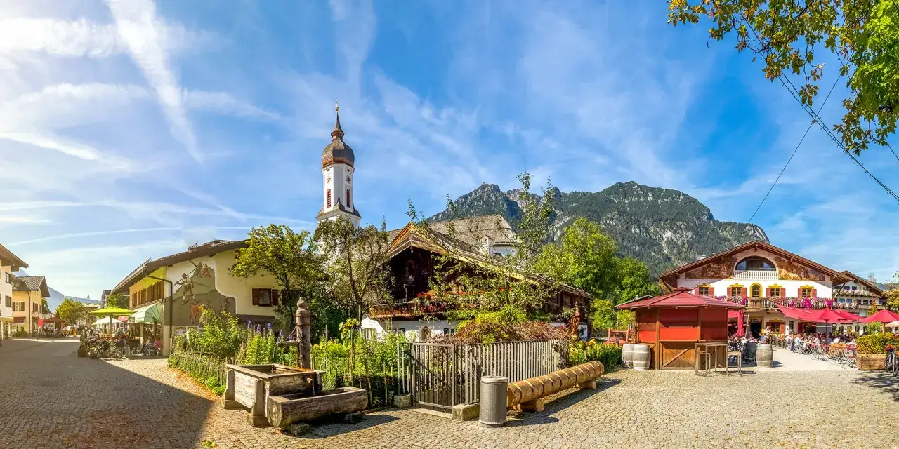 Idyllisches Dorf mit Kirche und Bergkulisse. Eine Szene, die an die Franken Geschichte erinnert, mit traditionellen Häusern und einem belebten Platz.
