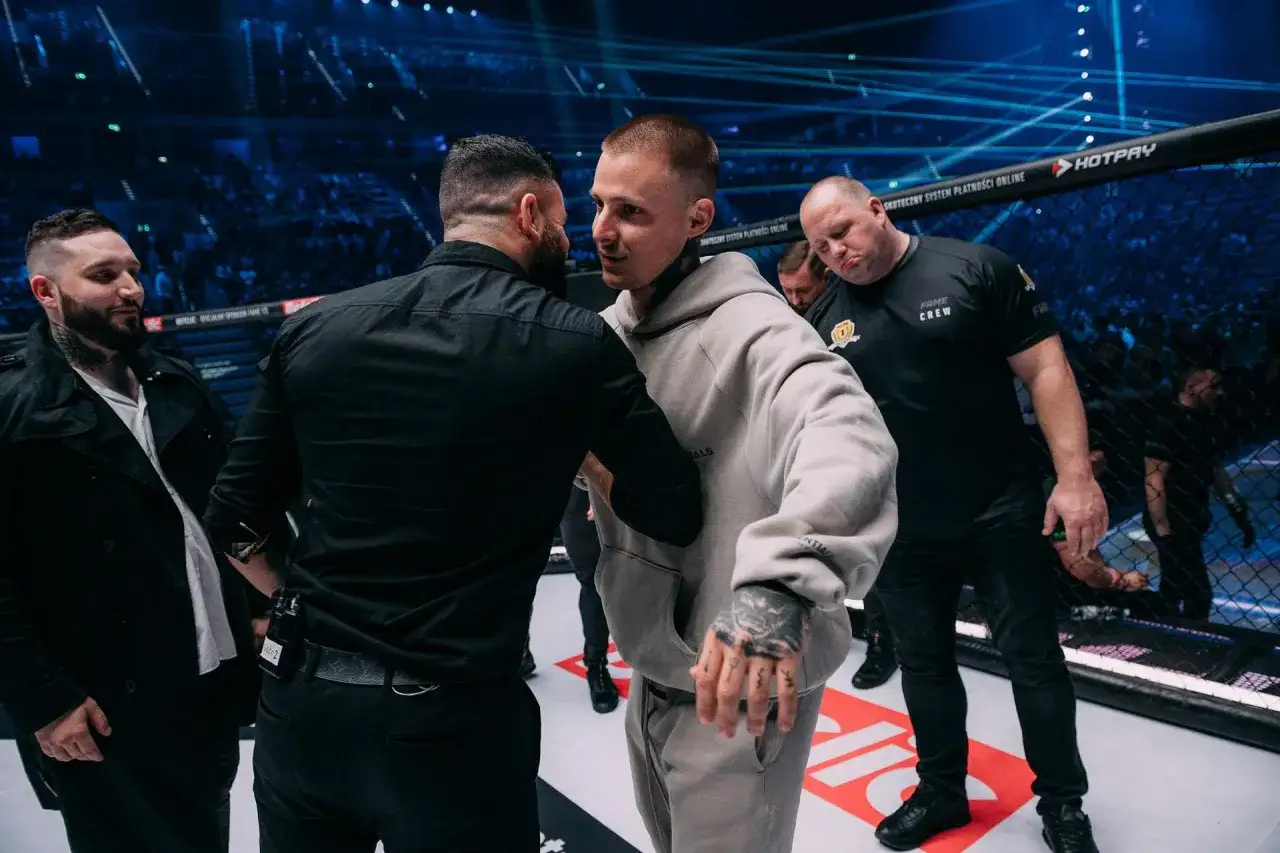 Mateusz Trąbka, młody zawodnik, w szarej bluzie, otoczony przez ochronę, po walce w klatce.