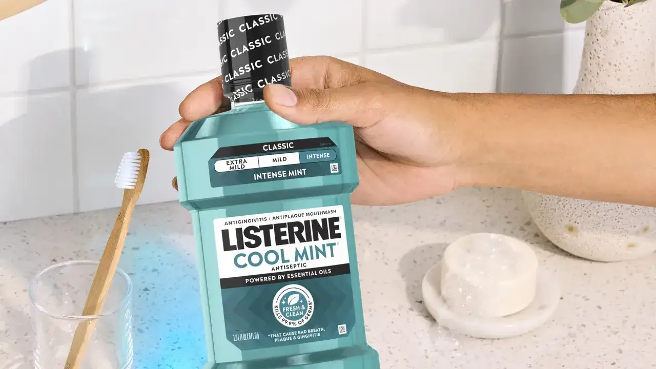 Mano sostiene Listerine Cool Mint. El listerine tiene clorhexidina, ideal para una higiene bucal completa. Cepillo de dientes y jabón cerca.